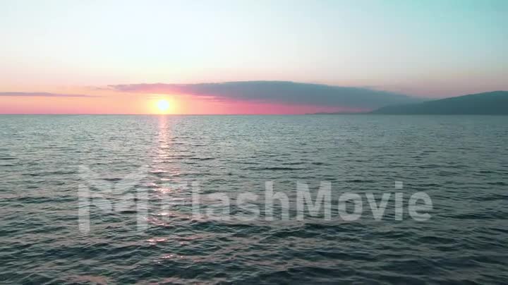 Aerial 4k view. Stunning sunset sun over the sea. Beautiful cinematic scene. Golden sun sets over the horizon, flying above the surface of the water in slow motion