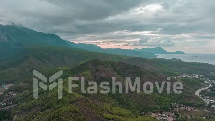 Aerial drone view. Flight over a residential area at the foot of the mountains. Green trees. Highway. Gray clouds.