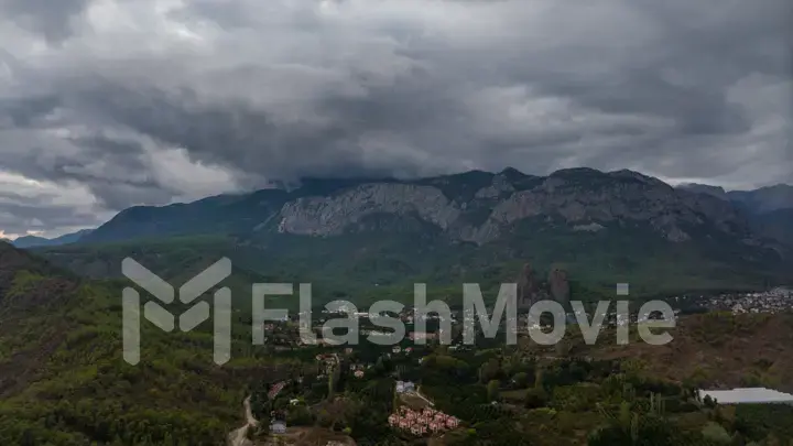 Aerial drone view of a hilly green area. Houses in the green forest. Overcast weather. Gray clouds. Photography