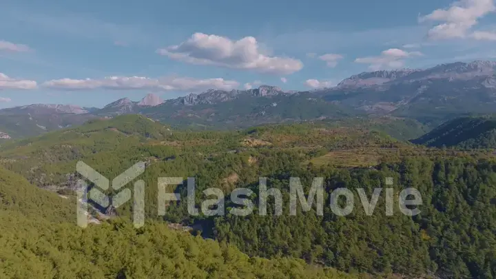 Top view. Aerial drone view of flight over the hills. Mountain landscape. Blue sky white clouds. Green trees.