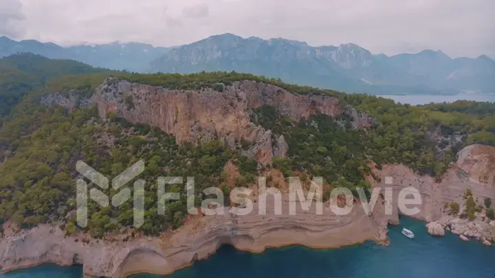 Flight over a large rocky island in the sea. The boat is sailing. Mountains in the background. Aerial drone view