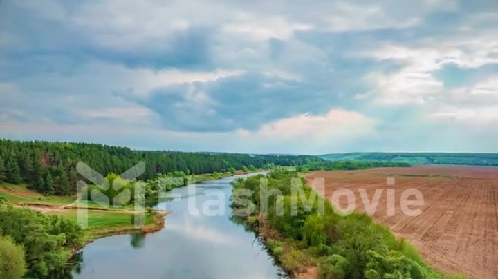 Wide shot on river, field, forest, clouds move in timelapse footage. Green landscape.