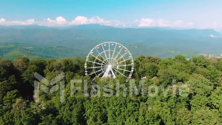 Aerial 4k view. A ferris wheel spins on top of a mountain. Stunning views of the mountains and the sea. Attraction for adults and children