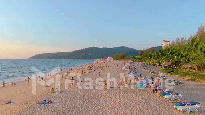PHUKET, THAILAND - 15 MAR 2020: Sunset on Karon beach, people swim in the sea and sunbathe, resort beach. A few days before closing beaches due to quarantine covid-19. Aerial 4k footage