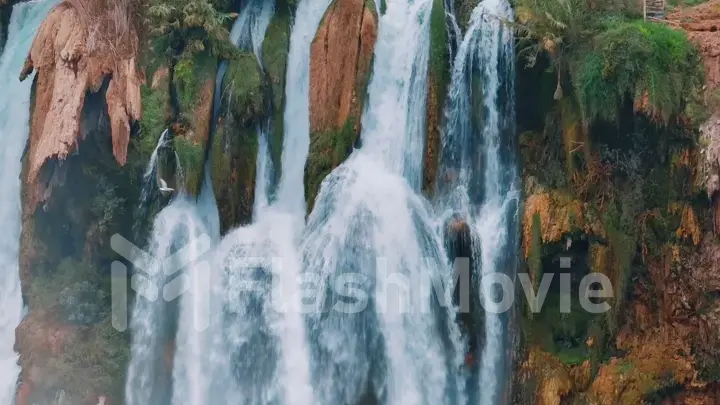 A bird flies in front of a stormy waterfall on a red rock. The element of water. Wildlife concept. Aerial drone view