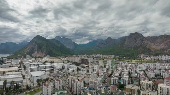 Top view of the big city. Residential houses. Urbanization. Green mountains and clouds in the background. Timelapse
