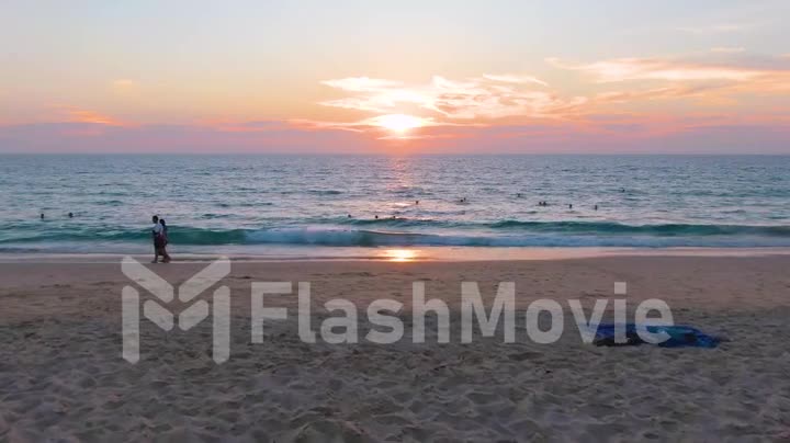 PHUKET, THAILAND - 15 MAR 2020: Sunset on Karon beach, people swim in the sea and sunbathe, resort beach. Aerial 4k footage