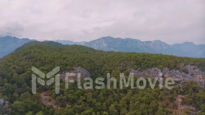 Cloudy weather. Aerial view of a rocky hill. Green trees. Human and nature. Mountain landscape.