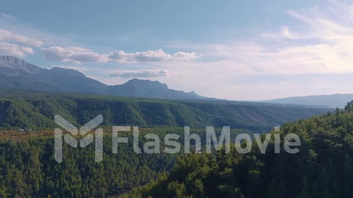 Top view. Aerial drone video footage of flight over the hills. Mountain landscape. Blue sky white clouds. Green trees.