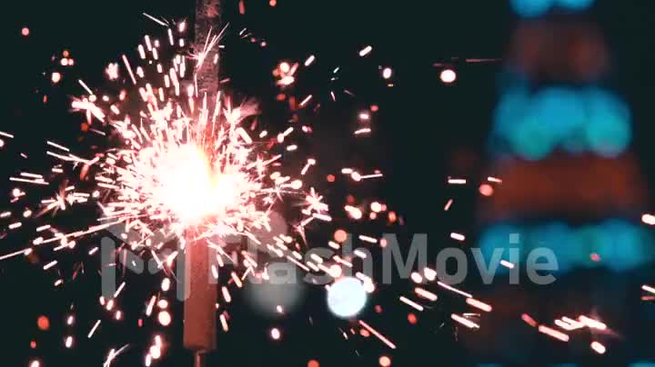 Bengal fire burning in slow motion against the background of a blinking Christmas tree
