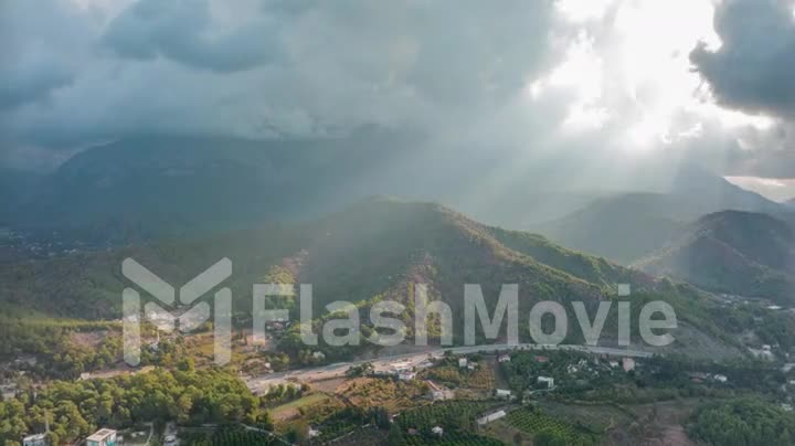 Sunbeams through the clouds. City under the mountain. Timelapse. Top view. Aerial drone video footage. Landscape.