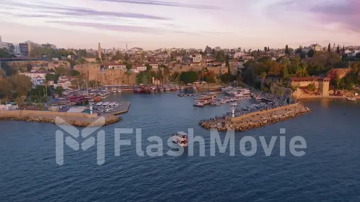 Flight over the seaport at sunset. Boats along the pier. Roofs. Water surface. Seascape. Aerial drone view