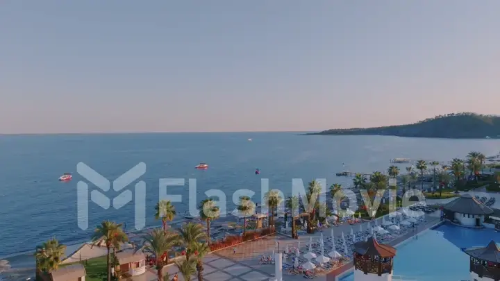 Panorama view flight over beach. Aerial drone view of a seascape. Palm trees, sand, beach umbrellas. Vacation