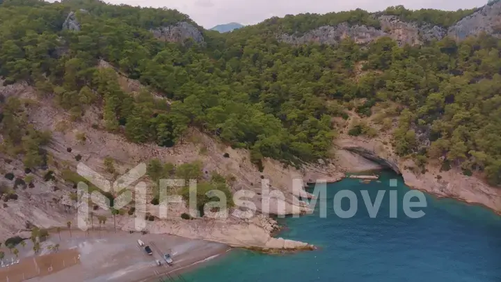 Top view of a rocky shore covered with green trees. Cave in the rock. Blue clear water. Seascape.