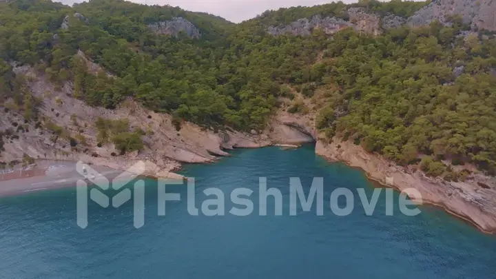 Flight over a large rocky island in the sea. The boat is sailing. Mountains in the background. Aerial drone view