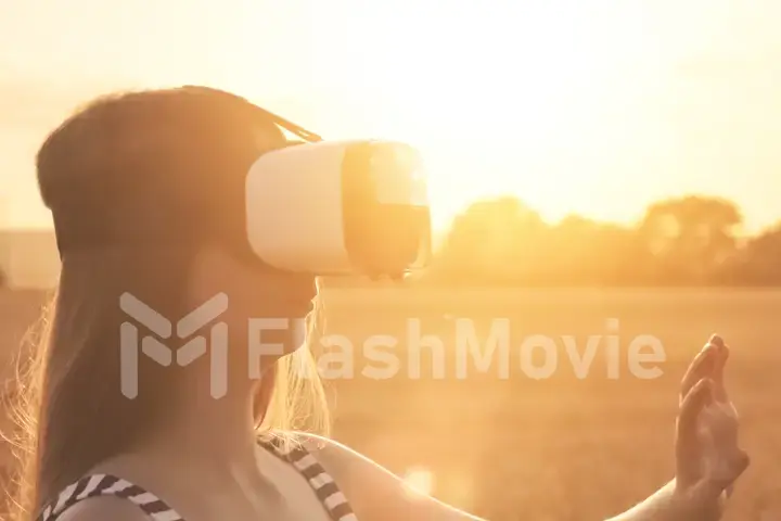 Beautiful girl in a golden wheat field uses virtual reality glasses in the sunset