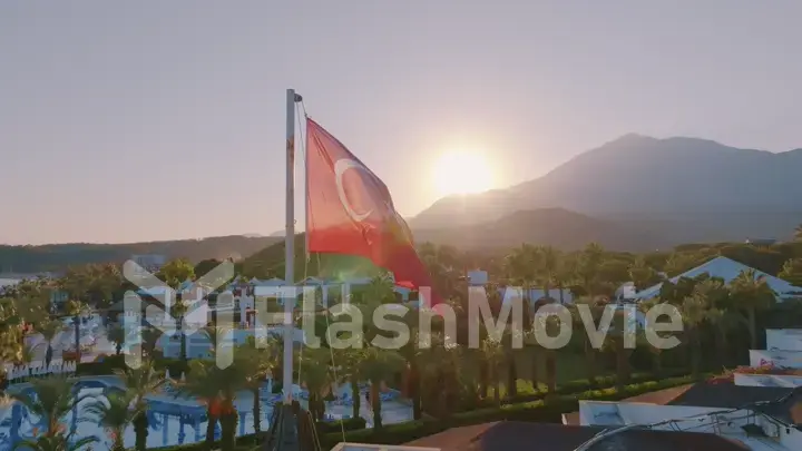 Aerial drone view of the flag flying on the roof. Sunset. Swimming pool, palm trees and mountains in the background