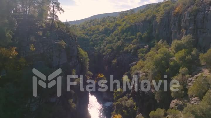 Aerial drone video footage flight over the shallow river bed between green rocks. Mountain landscape. Summer day