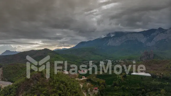 Aerial drone view. Flight over a residential area at the foot of the mountains. Green trees. Highway. Gray clouds.