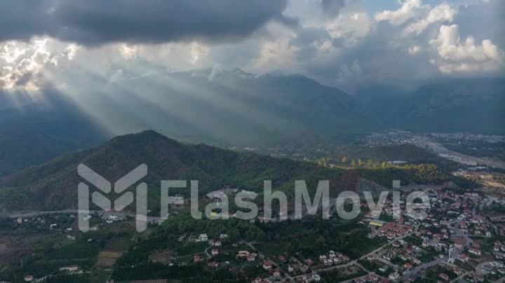 Sunbeams through the clouds. City under the mountain. Timelapse. Top view. Aerial drone video footage. Landscape.