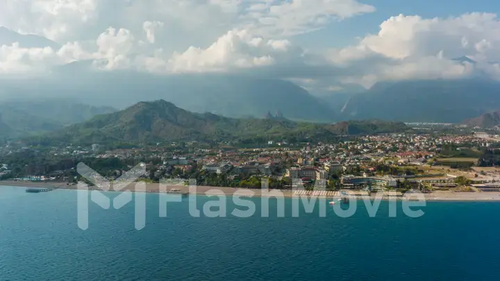 Aerial drone view of the city at the foot of the green mountains. Blue sky. White clouds. Green hills. Top view