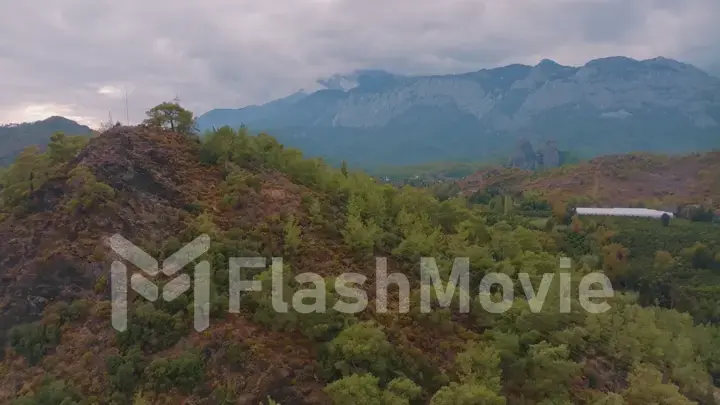 Cloudy weather. Aerial view of a rocky hill. Green trees. Human and nature. Mountain landscape. Photography