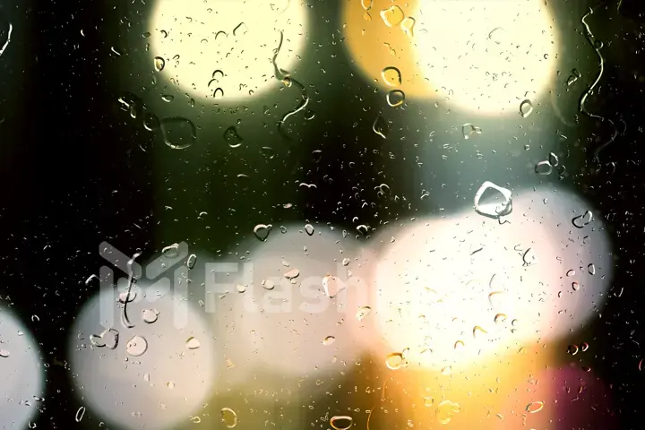 Drops of rain flow down the glass against the bokeh background of moving cars