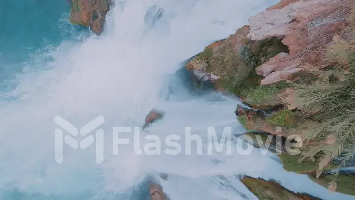 A stormy waterfall falls down from a cliff. Top view. Blue water. Foam. Rock. Wildlife. Aerial drone view