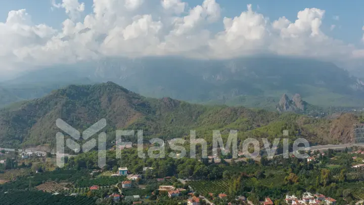 Aerial drone view of the city at the foot of the green mountains. Clear sunny day. White clouds. Green hills.