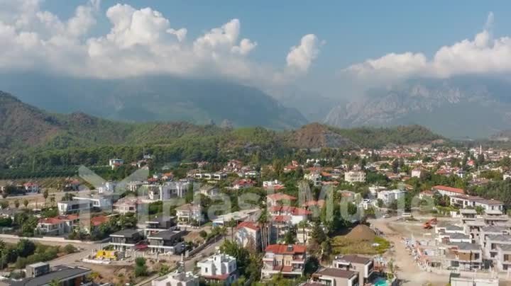 Drone footage of the city at the foot of the green mountains. Blue sky. White clouds. Green hills. Timelapse. Top view