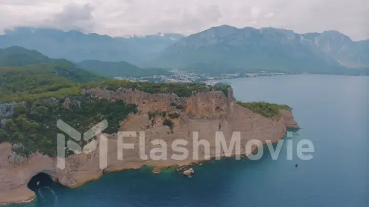 Top view of a rocky shore covered with green trees. Cave in the rock. The boat is near the shore. Aerial drone view