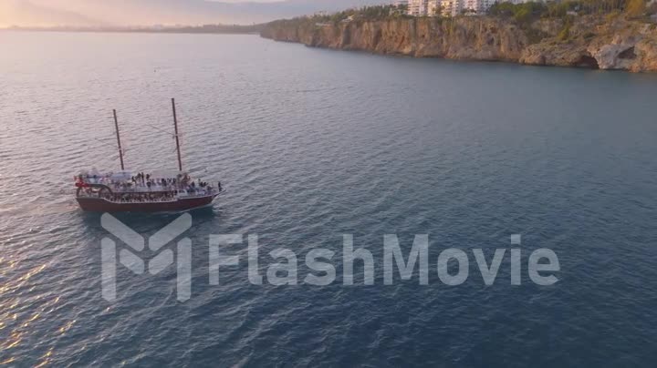Vintage sailing ship sails on the sea at sunset. Seascape. Rocky coast in the background. Aerial footage from a drone.