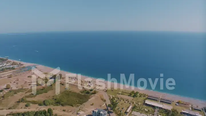 Top view of the coastline. Sea and sandy beach. Houses and hotels by the sea. Sun loungers and umbrellas on the beach.