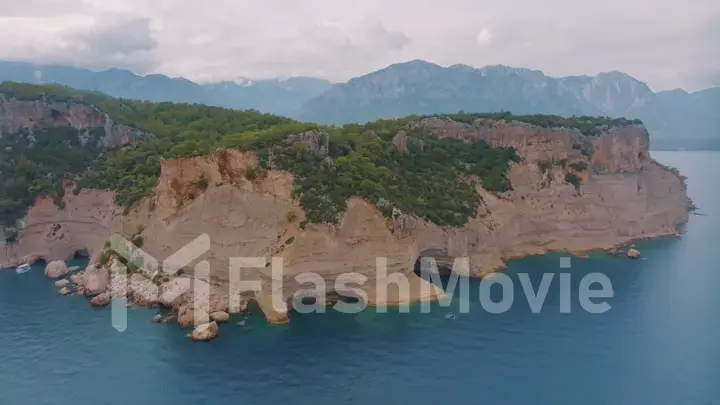 Top view of a rocky shore covered with green trees. Cave in the rock. Blue clear water. Seascape.