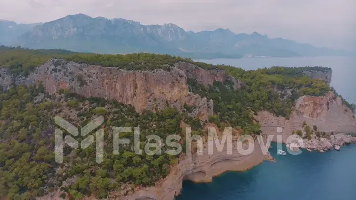 Flight over a large rocky island in the sea. The boat is sailing. Mountains in the background. Aerial drone view