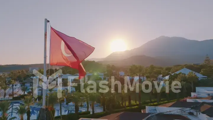 Turkish flag at sunset against the backdrop of the hotel. Swimming pool and palm trees. Mountain