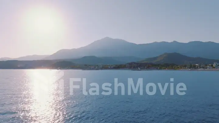 Aerial view flight over the blue sea at sunset. Beautiful clouds. Mountains in the background. Seascape. Photography