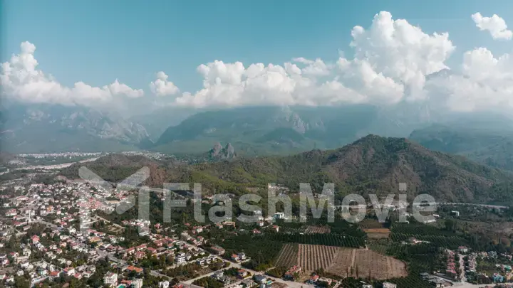 Aerial drone view of the city at the foot of the green mountains. Clear sunny day. White clouds. Green hills.