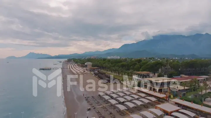 Panorama view flight over beach. Aerial drone view of a seascape. Palm trees, sand, beach umbrellas. Vacation