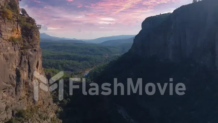 Aerial drone view of a large deep canyon. Sheer cliffs and green trees. Wildlife. Sunset background. Mountain river