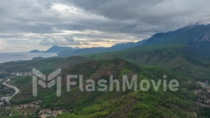 Aerial drone view of the city at the foot of the green mountains. It's a nasty day. Sunbeams between the clouds.