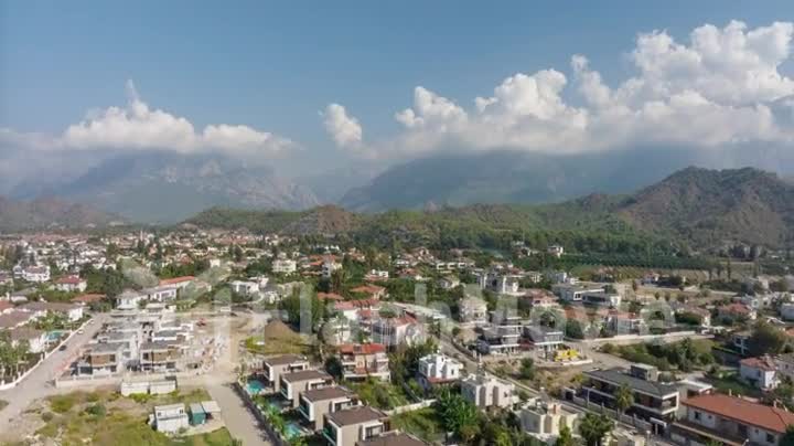 Flight over a small town on a sunny day. Green mountains and white clouds in the background. Aerial drone video footage