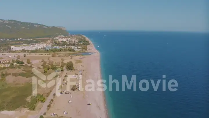 Top view of the coastline. Sea and sandy beach. Houses and hotels by the sea. Sun loungers and umbrellas on the beach.