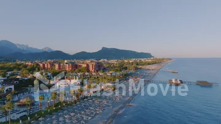 Aerial view of seascape at sunset. Pier. Sandy beach, umbrellas, sun loungers, palm. Mountains in the background