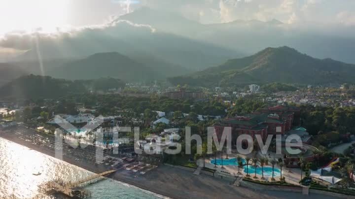 Aerial video footage from a drone of the city on the coast. Sunset. Green mountains. Residential houses. Timelapse