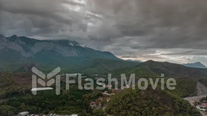 Top view of the hilly green area. Houses in the green forest. Timelapse. Overcast weather. Gray clouds. Photography.