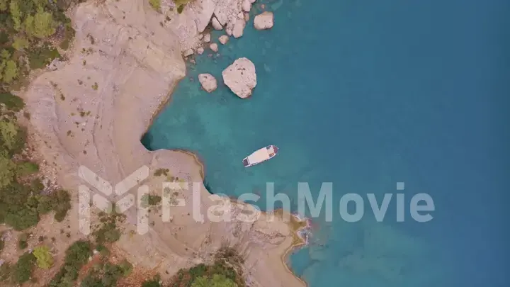 Top view of a rocky shore covered with green trees. Cave in the rock. The boat is near the shore. Aerial drone view