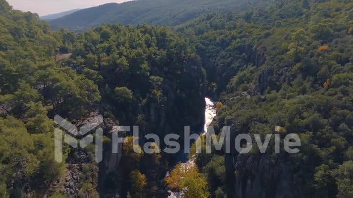 Flight over the shallow river bed between green rocks. Mountain landscape. Blue sky and clouds. Aerial drone footage