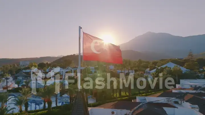 Aerial drone view of the flag flying on the roof. Sunset. Swimming pool, palm trees and mountains in the background