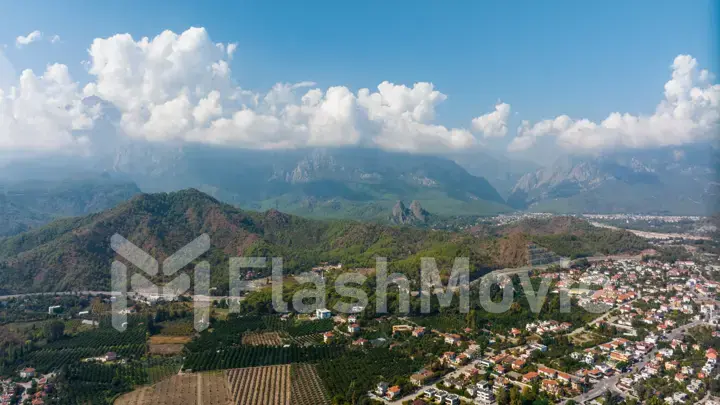 Aerial drone view of the city at the foot of the green mountains. Blue sky. White clouds. Green hills. Top view